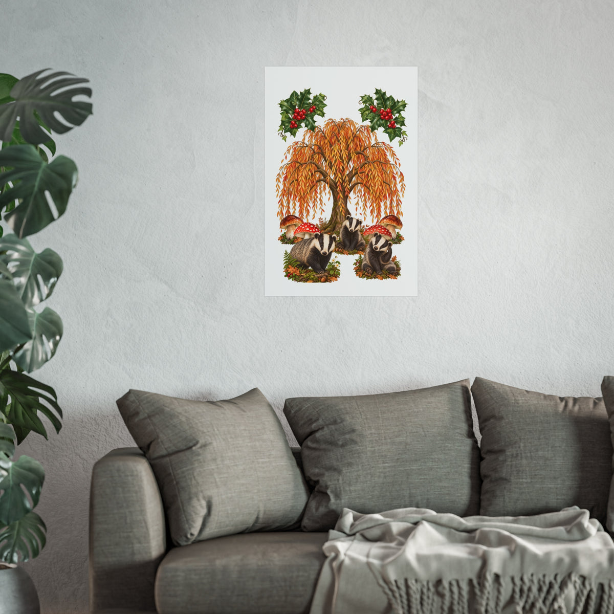 A framed wall art print featuring a whimsical autumn tree with orange leaves, badgers, and holly branches, displayed above a gray sofa in a living room setting.