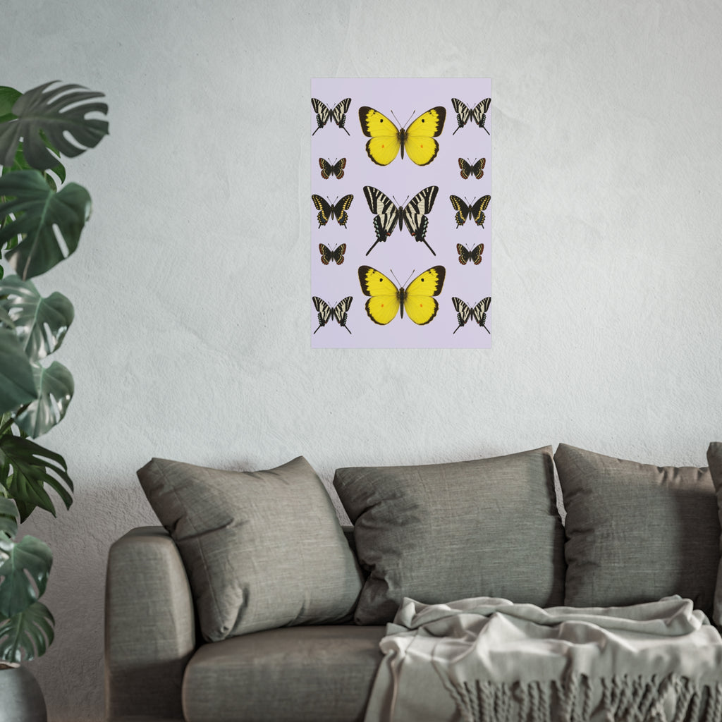 A vertical wall art print featuring yellow and black butterfly illustrations on a pale lavender background, displayed above a gray sofa in a living room setting with a plant on the left.
