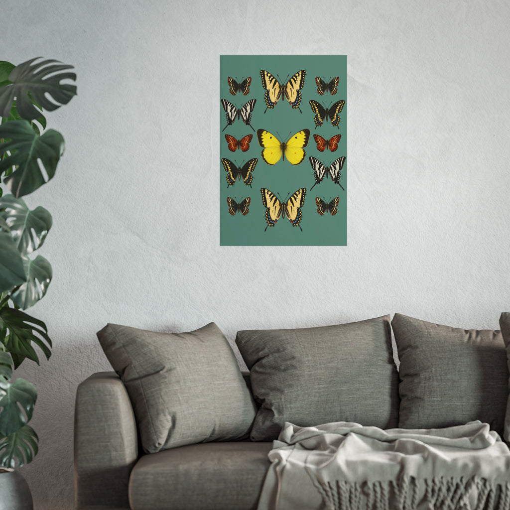 A vertical wall art print featuring a collection of colorful butterflies on a muted teal-green background, styled in a modern living room setting above a gray fabric sofa with a throw blanket and a potted green plant in the foreground.