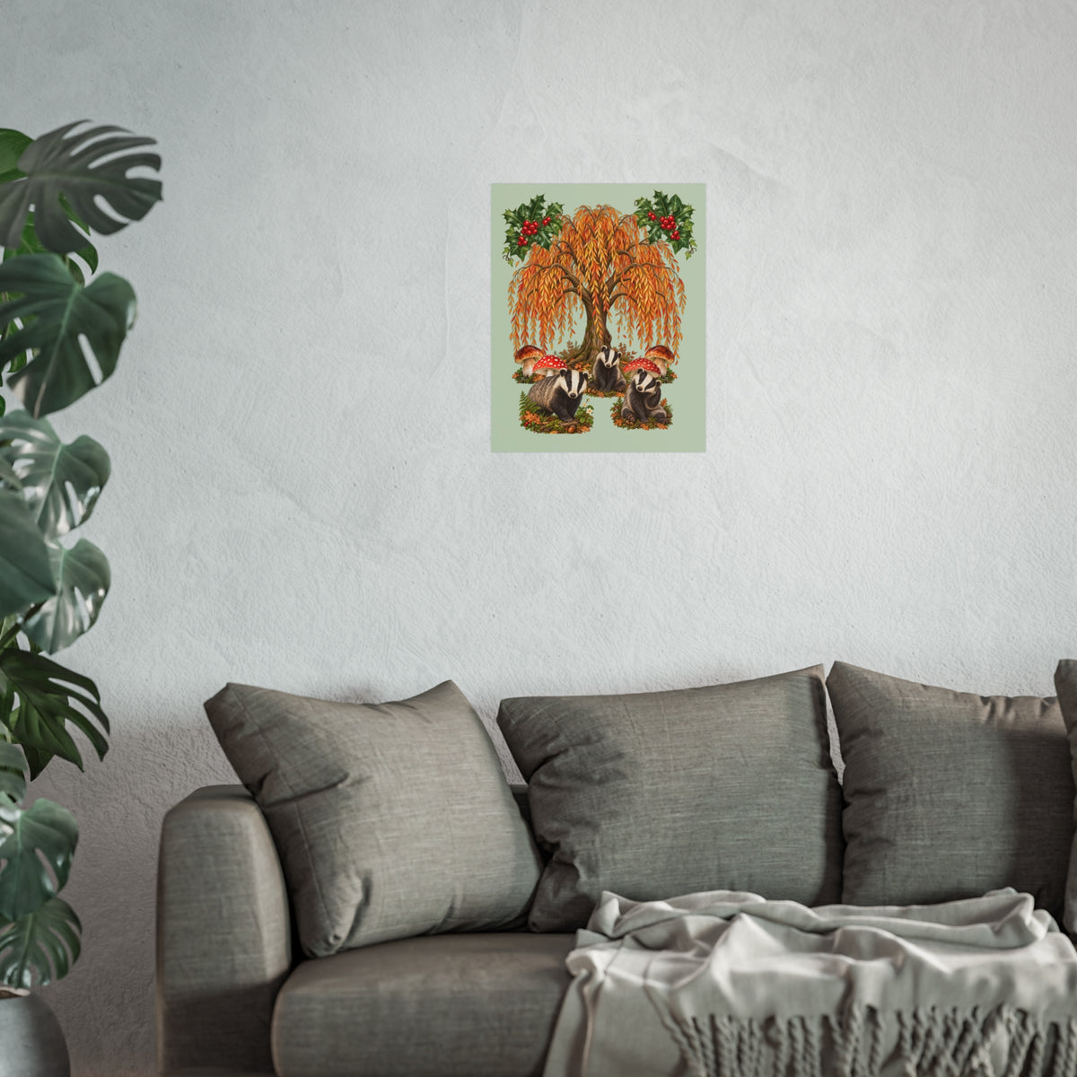 A framed wall art print featuring an autumn weeping tree with orange leaves and red berries, displayed above a gray sofa in a living room setting with a potted plant on the left.