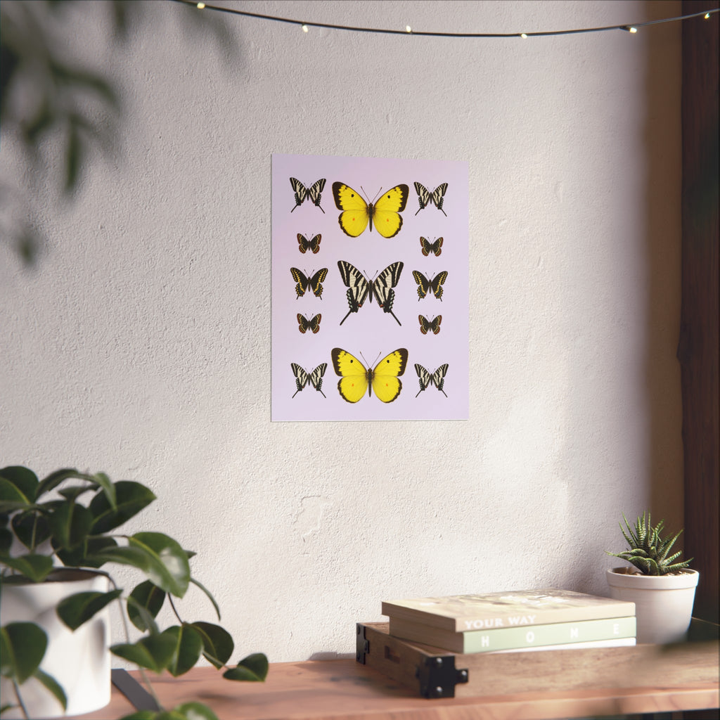 A vertical art print featuring various butterfly illustrations on a light lavender background, displayed on a textured white wall in a styled room setting with a wooden shelf, books, and potted plants.