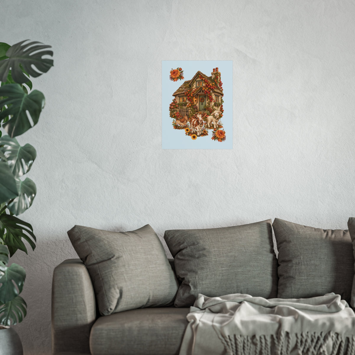 A cozy living room scene with a gray sofa, textured wall, and a small framed-style art print above it showing a decorated house with autumn leaves and pumpkins. A large green plant is visible on the left side.