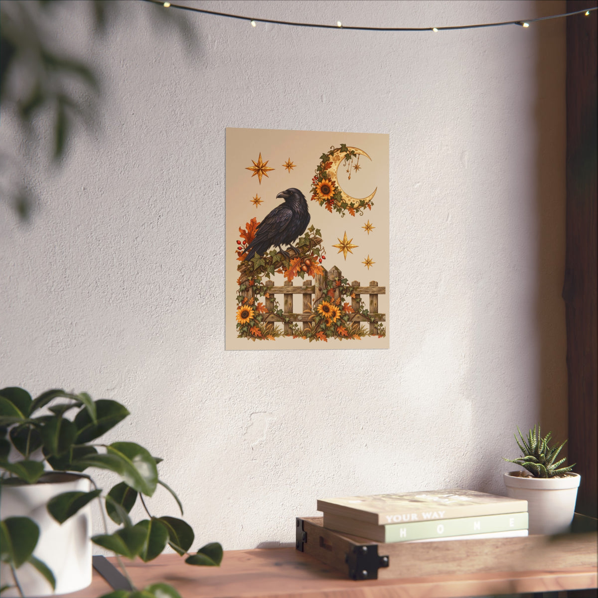 A vertical art print featuring a black raven perched on a fence with sunflowers and a crescent moon, displayed on a textured white wall above a wooden shelf with books and small potted plants.