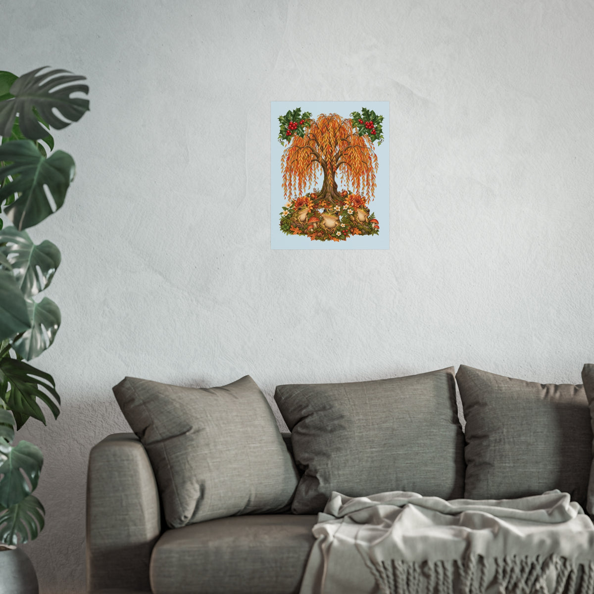 A framed or unframed wall art print depicting an autumn tree with orange and yellow foliage, red berries, and a light blue background, displayed above a gray sofa in a living room setting with a plant on the left.
