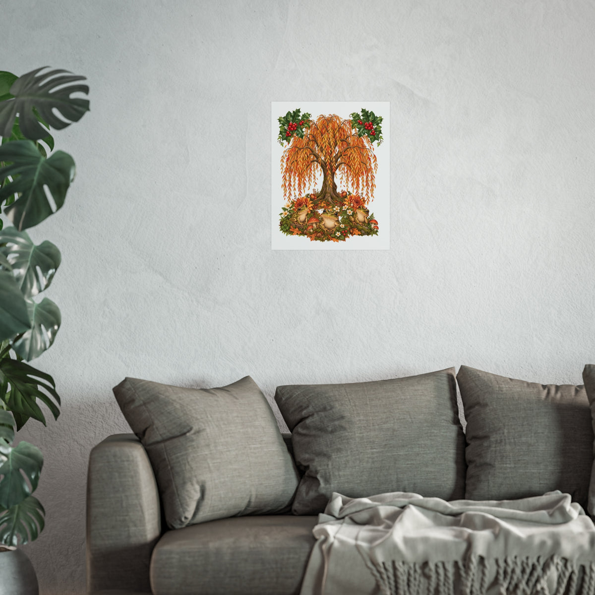 A framed wall art print featuring an autumn tree with orange and yellow leaves, red berries, and green foliage, displayed on a light gray wall above a gray sofa with pillows and a throw blanket, with a green plant on the left.