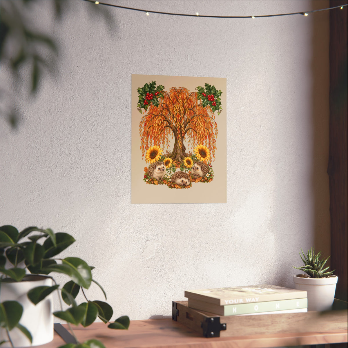 A vertical art print featuring a whimsical autumn tree with orange leaves, sunflowers, and small animals, displayed on a textured white wall above a wooden shelf with books and plants.