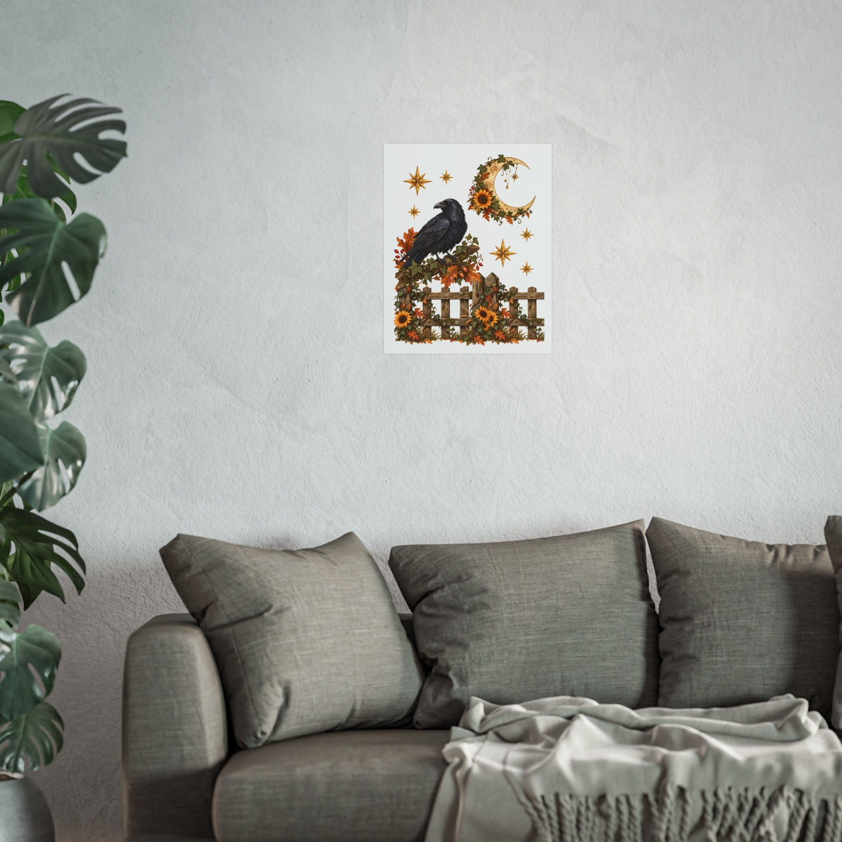 A small wall art print featuring a black raven perched on a fence with autumn leaves, stars, and a crescent moon, displayed above a gray sofa in a living room setting with a plant on the left.