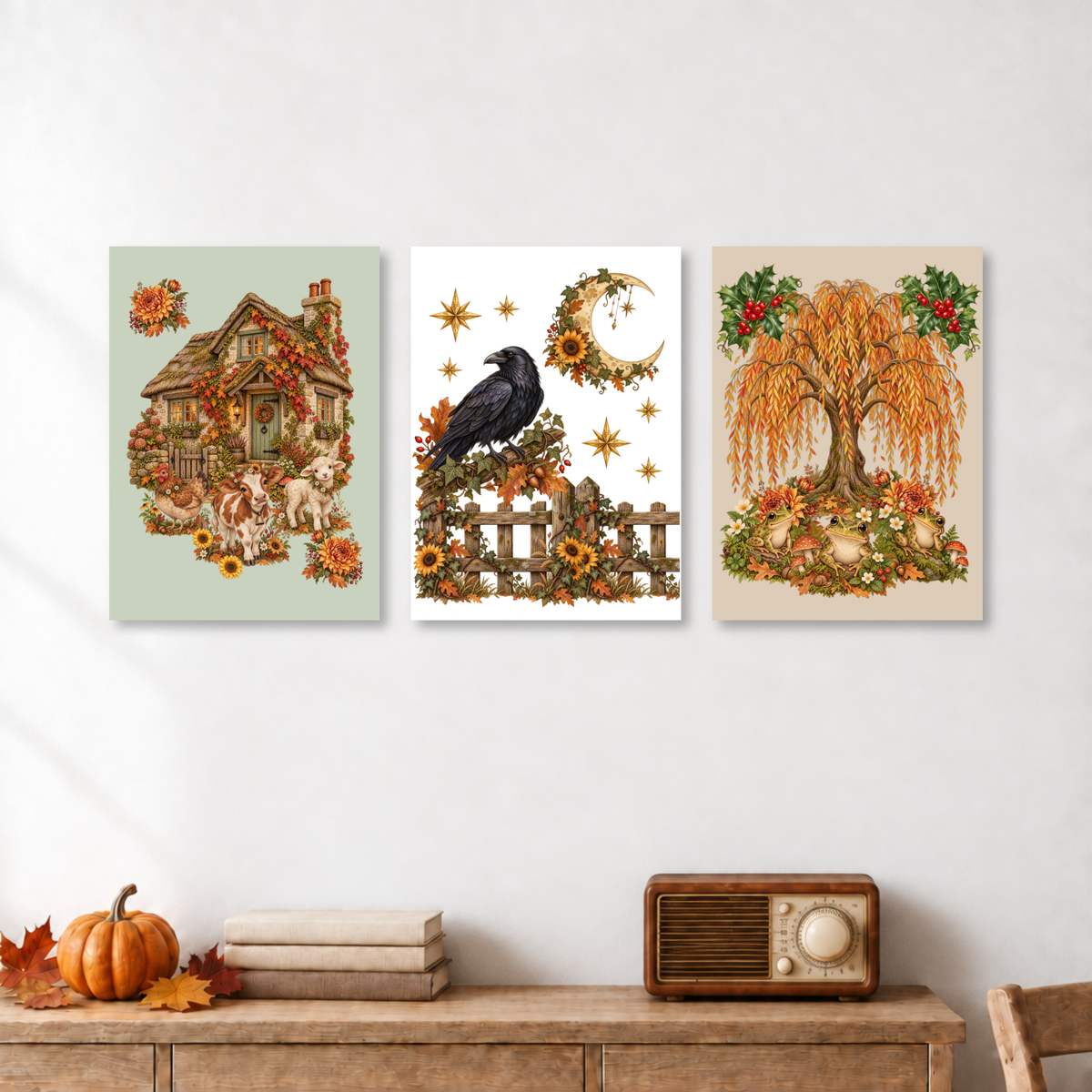 Three vertical autumn-themed art prints displayed side-by-side on a white wall above a wooden console table with a pumpkin, books, and a vintage radio.