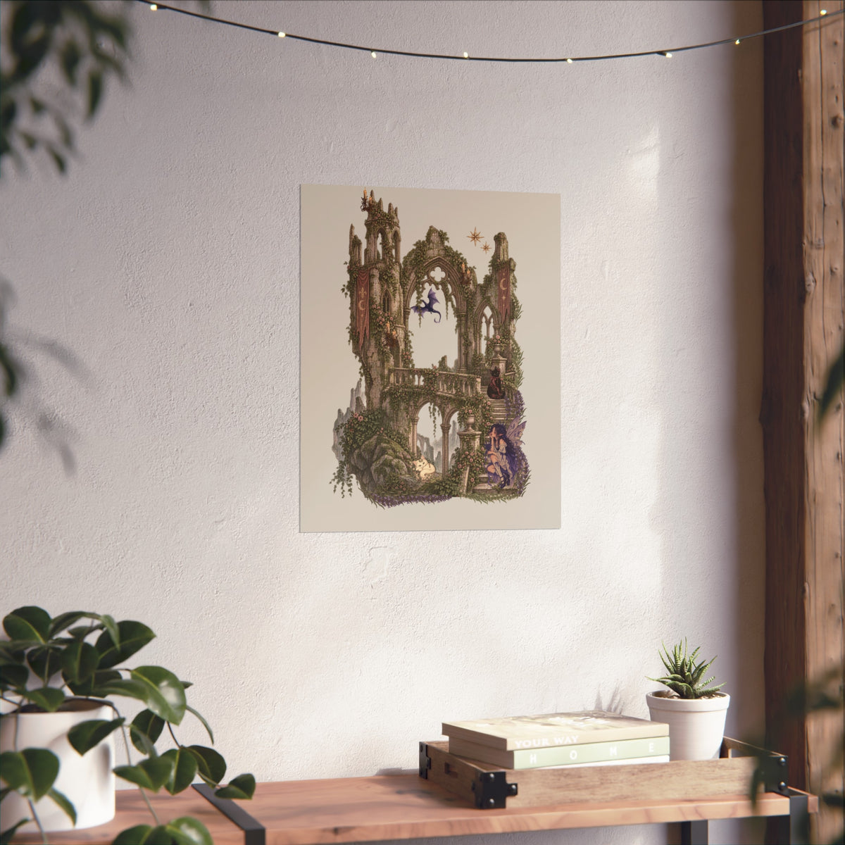 A vertical art print featuring a whimsical, fantasy-style illustration of a stone archway and tower structure in earthy greens and browns, set against a pale blue background. The print is displayed on a textured off-white wall above a wooden console table decorated with books, a small succulent, and potted plants.