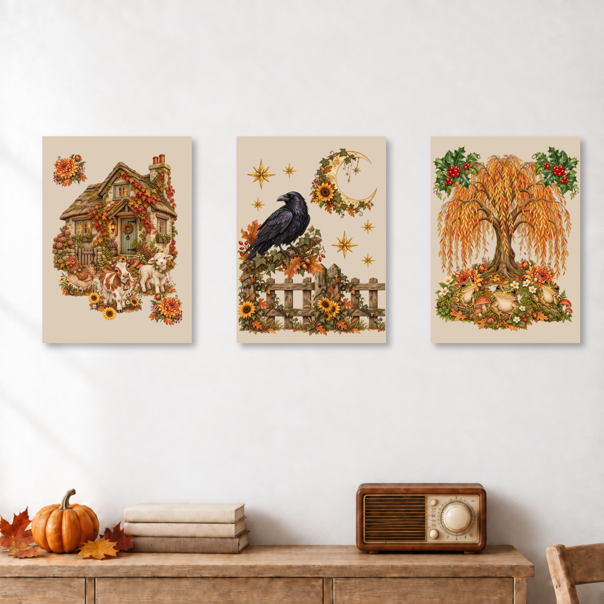Three vertical autumn-themed art prints displayed side-by-side on a white wall above a wooden console table. The prints feature vintage illustrations: a cozy house with a dog on the left, a raven on a fence under a crescent moon in the center, and an autumn weeping tree with pumpkins on the right.